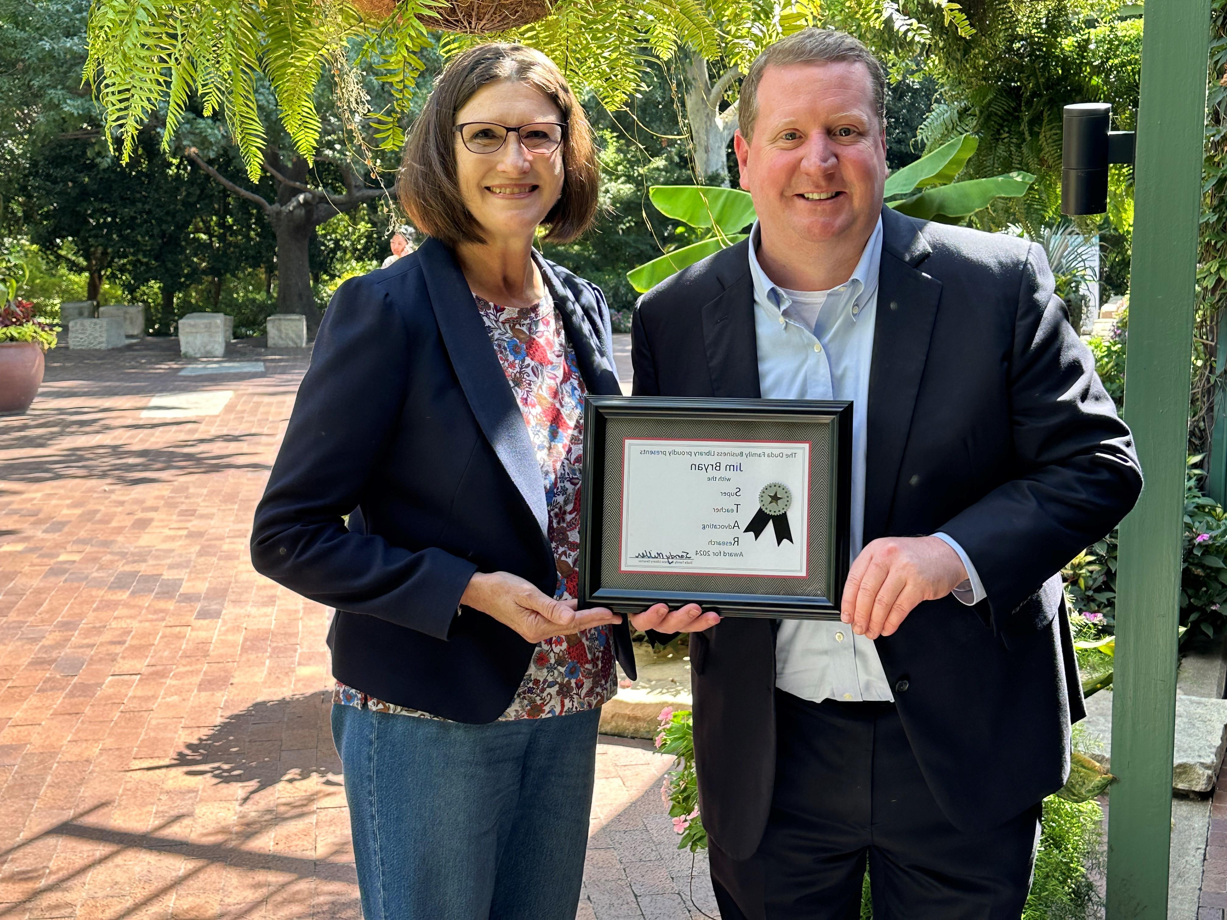 Jim Bryan, Associate Dean of BBA Undergraduate Program, holding the Duda Family Business Library's framed STAR Award with Sandy Miller, Director of the Duda Family Business Library